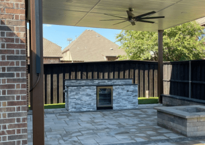 A narrow side yard walkway featuring large square concrete pavers set into a lush artificial turf path, bordered by white river rock and a tall wooden privacy fence.
