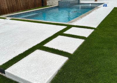 A large modern swimming pool with a stone-clad spa next to a rustic wood gabled pavilion and a geometric concrete paver and artificial turf deck.
