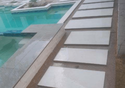 Modern backyard pool area featuring a geometric swimming pool and integrated hot tub surrounded by large square white concrete pavers set in a grey gravel base.