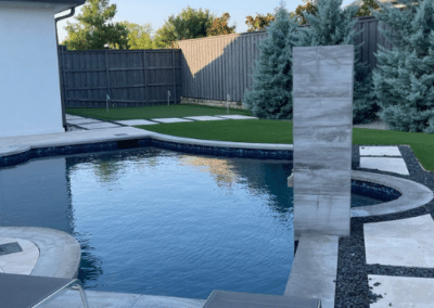 Modern black aluminum louvered pergola featuring an integrated ceiling fan, wall-mounted flat-screen TV, and recessed lighting on a stone patio.